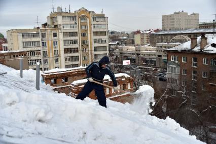 Новосибирск. Дворник  на крыше лопатой счищает снег.