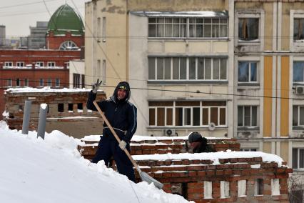 Новосибирск. Дворник на крыше лопатой счищает снег.