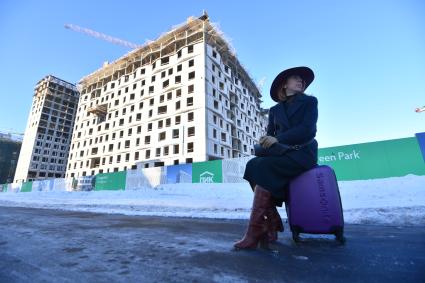 Москва.  Девушка сидит на чемодане  рядом с новостройкой.