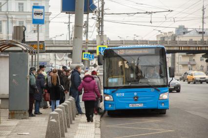 Москва.  Пассажиры садятся в автобус на остановке общественного транспорта.