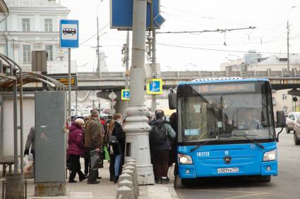 Москва.  Пассажиры садятся в автобус на остановке общественного транспорта.