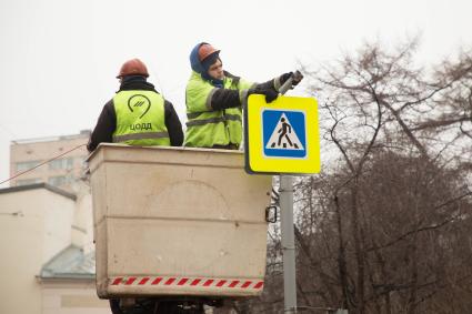 Москва. Сотрудники ЦОДД монсируют дорожный знак`Пешеходный переход`.