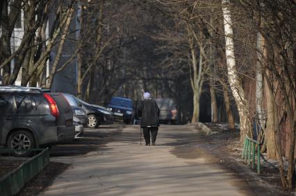 Москва.  Женщина с тростью на прогулке во дворе жилого дома   в районе Матвеевское.