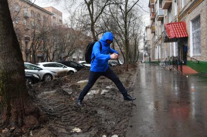 Москва. Мужчина перешагивает через грязные лужи.