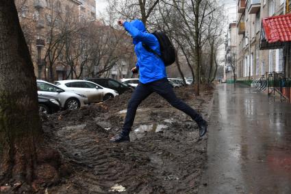 Москва. Мужчина перешагивает через грязные лужи.