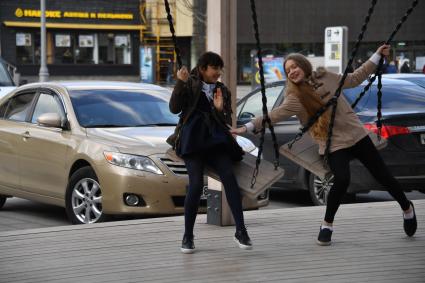 Москва. Девочки качаются на качелях на Новом Арбате.