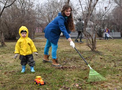 Москва. Женщина с ребенком  на общегородском субботнике `За чистоту икусства` в парке  `Музеон` убирает сухие листья с газона.