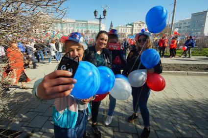 Екатеринбург. Девушки фотографируются на фоне первомайской демонстрации перед началом шествия колонны профсоюзов в день весны и труда.