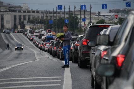 Москва. Мужчина торгует цветами на дороге среди машин.