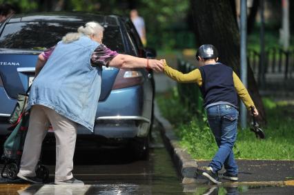 Москва.  Женщина с ребенком обходят лужу на тротуаре.