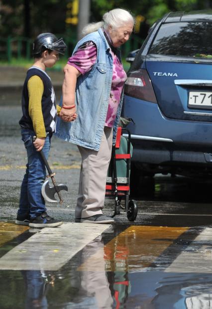 Москва.  Женщина с ребенком обходят лужу на тротуаре.