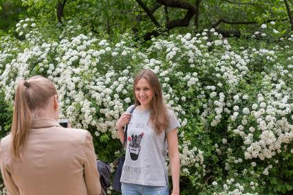 Москва.  Девушки фотографируются на фоне цветущих кустов в саду  Аптекарского сада.