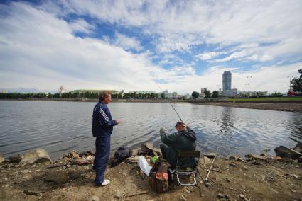 Екатеринбург. Мужчины ловят рыбу на обмелевшем  берегу набережной городского пруда.