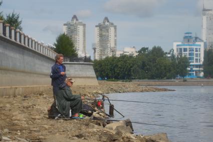 Екатеринбург. Мужчины ловят рыбу на обмелевшем  берегу набережной городского пруда.