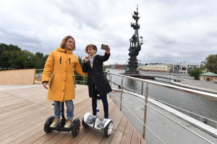 Москва.  Девушки на гироскутерах фотографируются  у  памятника Петру I на  Крымской  набережной.