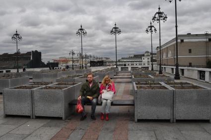 Москва.  Женщина и мужчина сидят на скамейках у Патриаршего моста.