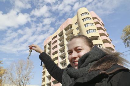 Барнаул. Девушка держит в руке ключи от квартиры на фоне многоэтажного жилого дома.