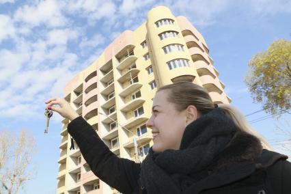 Барнаул. Девушка держит в руке ключи от квартиры на фоне многоэтажного жилого дома.