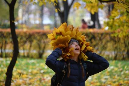 Москва.   Девочка примеряет на голову венок из осенних листьев.