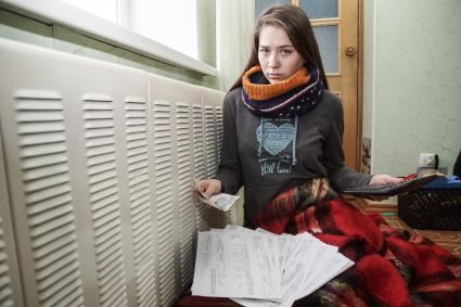Самара. Девушка изучает квитанции на оплату коммунальных платежей сидя у батареи.
