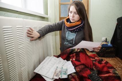 Самара. Девушка изучает квитанции на оплату коммунальных услуг сидя у батареи.