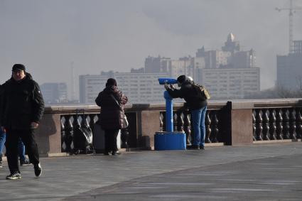 Москва.  Мужчина смотрит в бинокль на смотровой площадке Воробьевых гор.