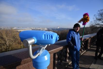 Москва.  Мужчина стоит рядом с биноклем  на смотровой площадке Воробьевых гор.