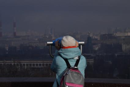 Москва.  Женщина смотрит в бинокль на смотровой площадке Воробьевых гор.