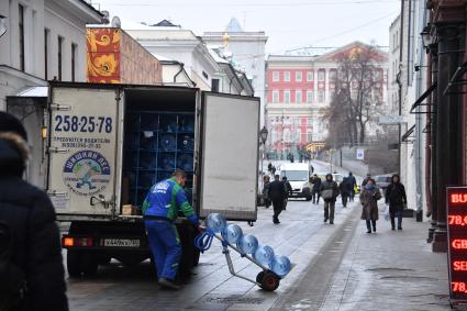 Москва.  Рабочий грузит бутыли из-под воды в грузовую машину в Столешниковом переулке.