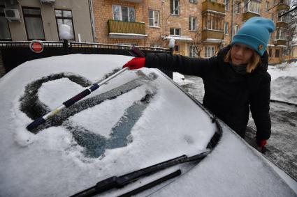 Москва. Девушка очищает машину от снега.