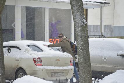 Тула.  Молодой человек  очищает машину от снега.