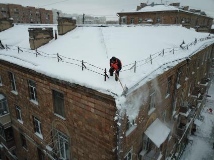 Москва.   Сотрудник коммунальной службы счищает снег с крыши дома.