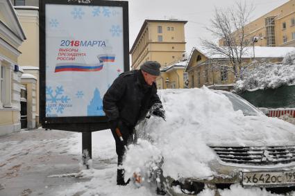 Москва.  Мужчина очищает машину от снега.