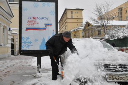 Москва.  Мужчина очищает машину от снега.