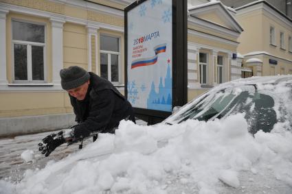 Москва. Мужчина очищает машину от снега.