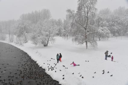 Москва. Дети кормят птиц у водоема в парке.