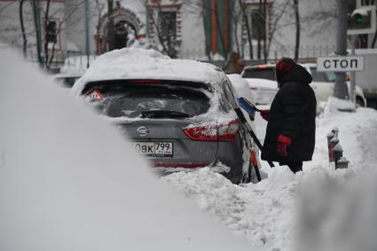 Москва. Женщина очищает машину от снега.