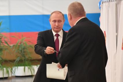 Москва. Действующий президент РФ, кандидат на пост президента РФ Владимир Путин (в центре) во время голосования на выборах президента РФ на избирательном участке # 2151.