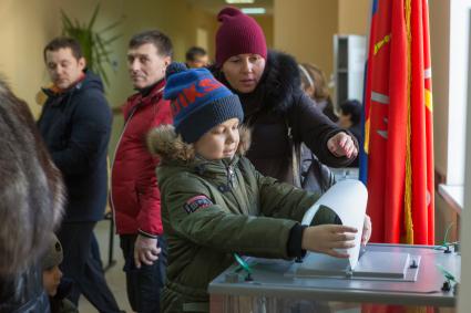 Санкт-Петербург.  Мальчик опускает бюллетень  в урну  для голосования  во время выборов президента России.