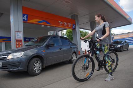 Самара.  Девушка с велосипедом на автозаправочной станции.