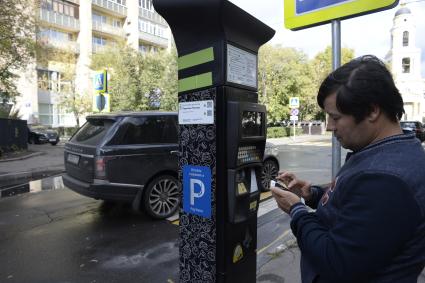 Москва. Мужчина оплачивает парковку автомобиля через паркомат.