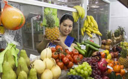 Иркутск.  Девушка торгует овощами и фруктами на рынке.