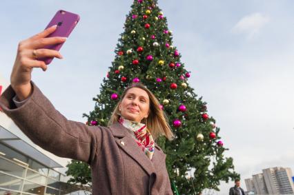 Санкт-Петербург. Девушка делает селфи на фоне новогодней елки на проспекте Маршала Жукова.