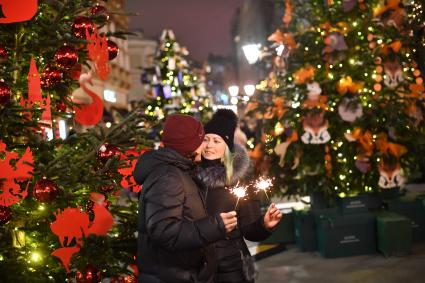 Москва.  Молодые люди среди елок, украшенных к Новому году, на Кузнецком мосту.