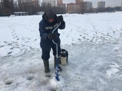 Московская область. Мужчина сверлит лунку для подледного лова.