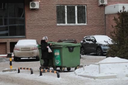 Красноярск.   Женщина выбрасывает мусор в мусорный контейнер.