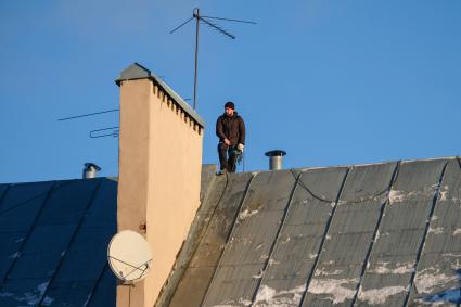 Санкт-Петербург. Сотрудник коммунальных служб счищает снег с крыши дома.