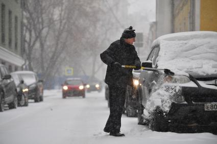 Москва. Мужчина очищает машину от снега   в Хлебном переулке.