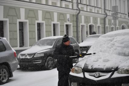 Москва. Мужчина очищает машину от снега   в Хлебном переулке.
