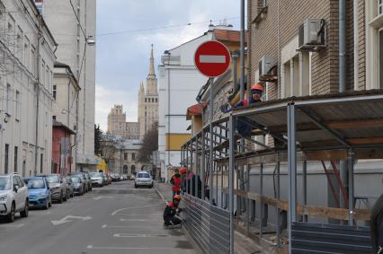 Москва.  Рабочие строят ограждение с навесом на одной и улиц города.